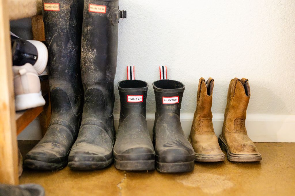 Three generations of Valley family boots — tall Hunter rain boots, kids' wellies, and worn cowboy boots lined up in a mudroom